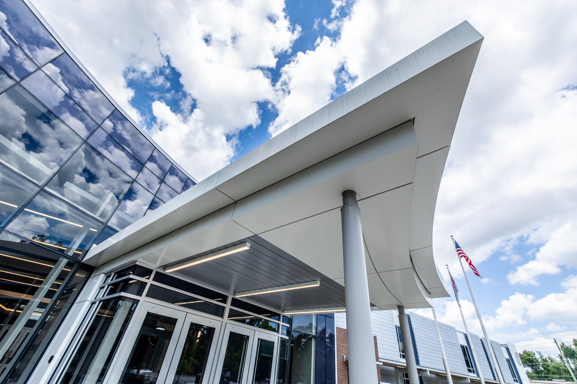 A curved steel canopy reflecting a bright cloud-filled sky