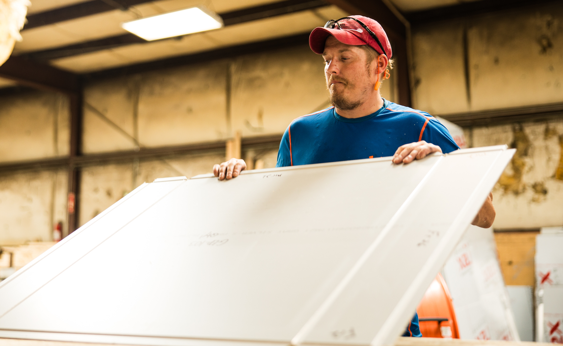A worker inspecting a large white panel in the fabrication shop